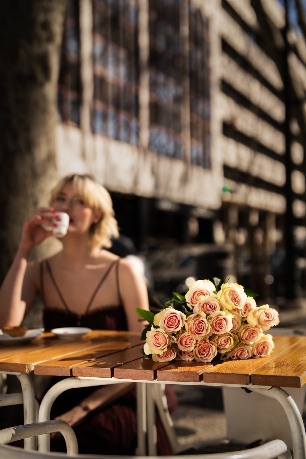 Ramo de rosas cor-de-rosa sobre a mesa de uma esplanada, junto a uma mulher.