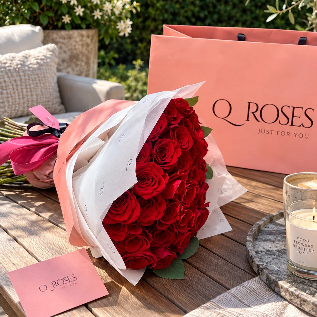 Luxury bouquet of 50 red roses with pink and white wrapping, displayed beside a QRoses gift bag.