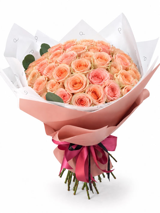 Bouquet da QRoses com 50 rosas em tons de pêssego, damasco e blush, envolvido em papel rosa e branco com fita da marca.