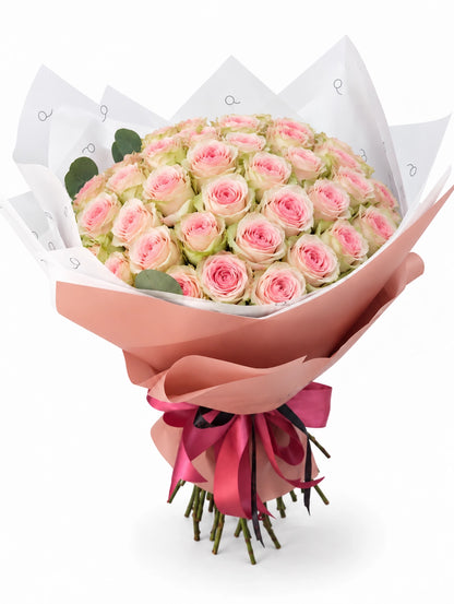 Bouquet da QRoses com 50 rosas rosa suave estilo Frutteto, com pétalas exteriores esverdeadas, envolvido em papel rosa e branco com fita da marca.