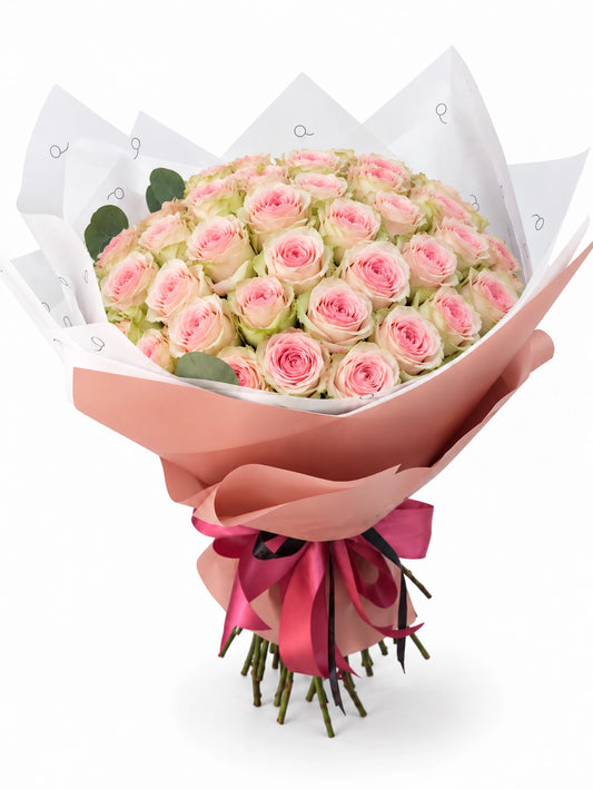 Bouquet da QRoses com 50 rosas rosa suave estilo Frutteto, com pétalas exteriores esverdeadas, envolvido em papel rosa e branco com fita da marca.