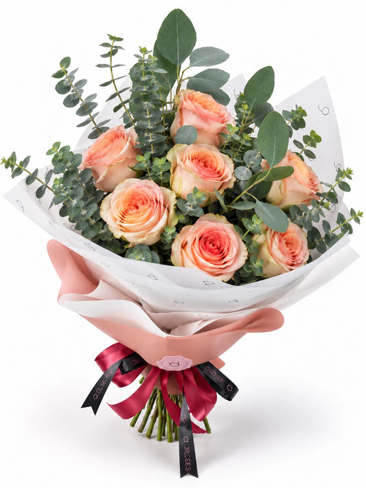 Essential da QRoses com rosas em tons de pêssego e eucalipto, envolvido em papel rosa e branco com fita da marca.