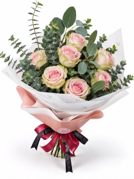 Bouquet Essential da QRoses com rosas rosa suave e eucalipto, envolvido em papel rosa e branco com fita da marca.