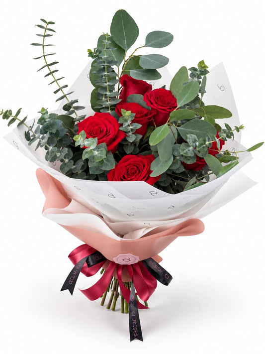 Bouquet Essential da QRoses com rosas vermelhas e eucalipto, envolvido em papel rosa e branco com fita da marca.