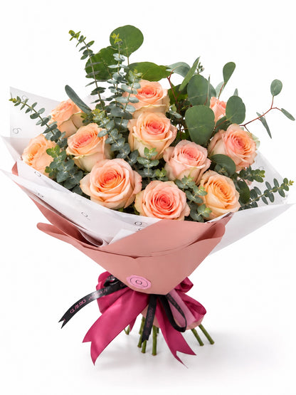 Bouquet Premium da QRoses com 12 rosas em tons de pêssego e eucalipto, envolvido em papel rosa e branco com fita da marca.