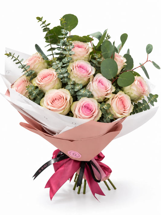 Bouquet Premium da QRoses com 12 rosas rosa suave e eucalipto, envolvido em papel rosa e branco com fita da marca.