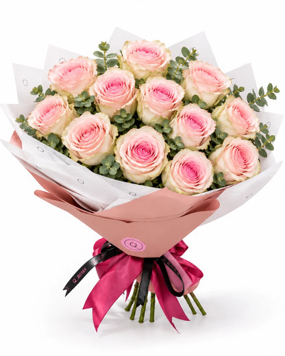 Bouquet premium QRoses com 13 rosas Frutetto rosa e eucalipto, envolvido em papel rosa empolvado e branco, com laço fúcsia.