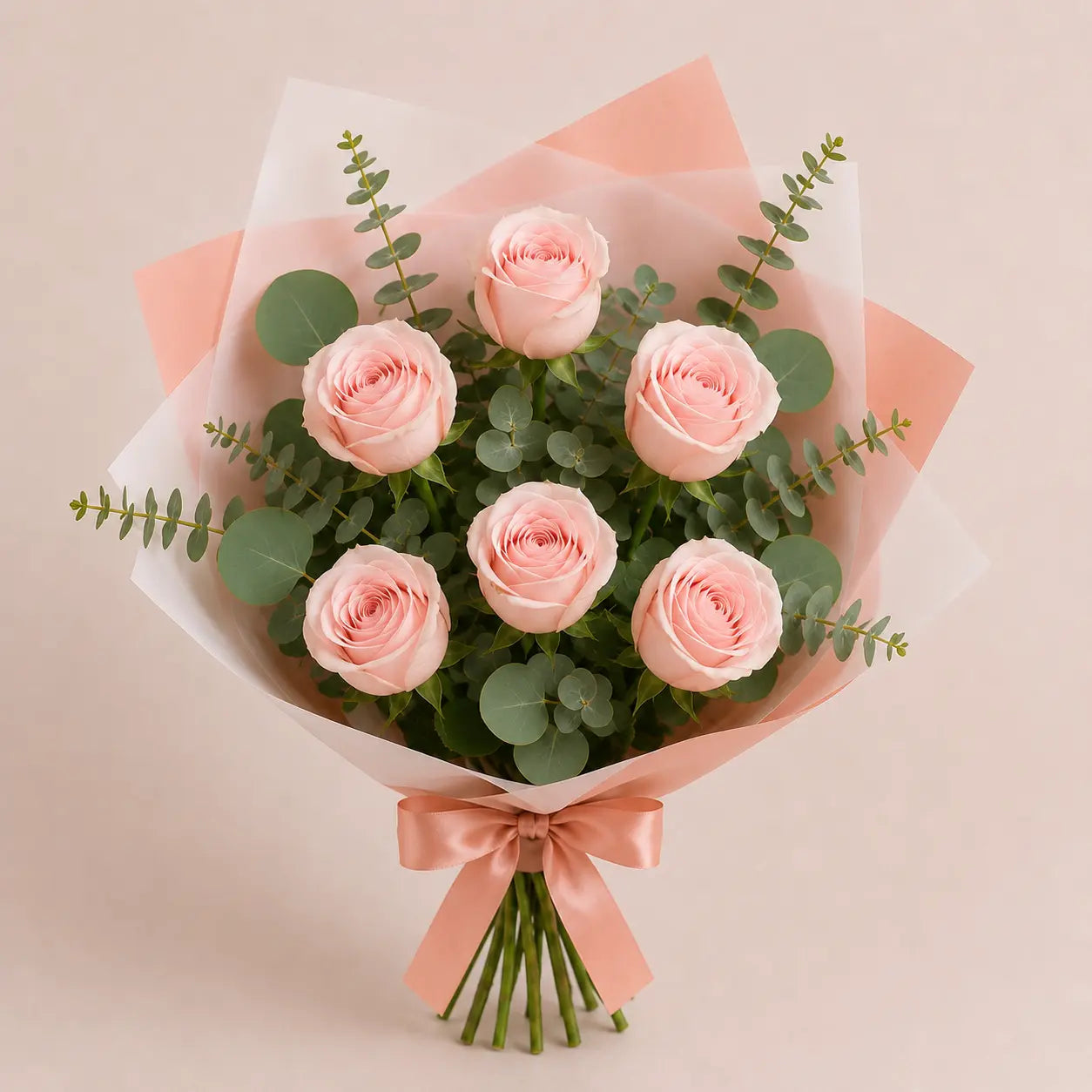 Ramo Essencial de 5 ou 6 rosas cor-de-rosa envolvidas em papel artístico branco e rosa, com eucalipto e laço acetinado rosa, fotografado em vista superior sobre fundo neutro.