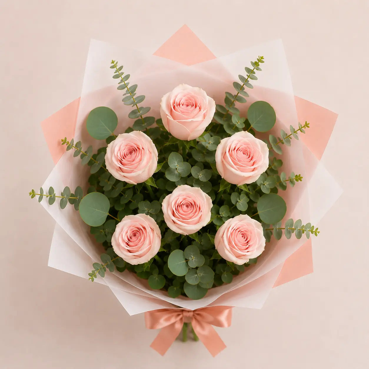 Vista superior do Ramo Essencial de 5 ou 6 rosas cor-de-rosa, envolvidas em papel artístico branco e rosa, com eucalipto e laço acetinado rosa sobre fundo neutro.