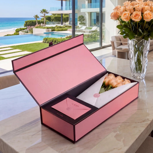 Caixa Signature Box QRoses com rosas pêssego premium, cartão QR e envelope elegante sobre mesa de mármore com vista para o mar.