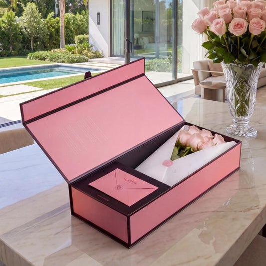Caixa Signature Box QRoses com rosas cor-de-rosa premium, cartão QR e envelope elegante, apresentada sobre mesa de mármore num ambiente luminoso e sofisticado.