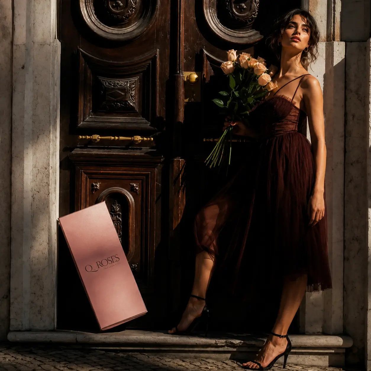 Mulher elegante com bouquet de rosas cor-de-rosa premium QRoses ao lado da caixa Signature Box, num cenário sofisticado com estilo editorial de luxo.