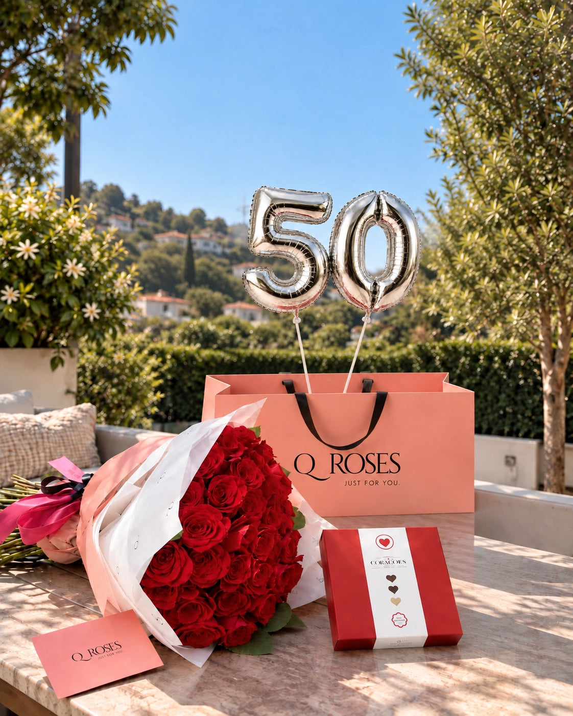 Ramo de 50 rosas vermelhas QRoses com balões prateados 50 e chocolates Arcádia em ambiente exterior