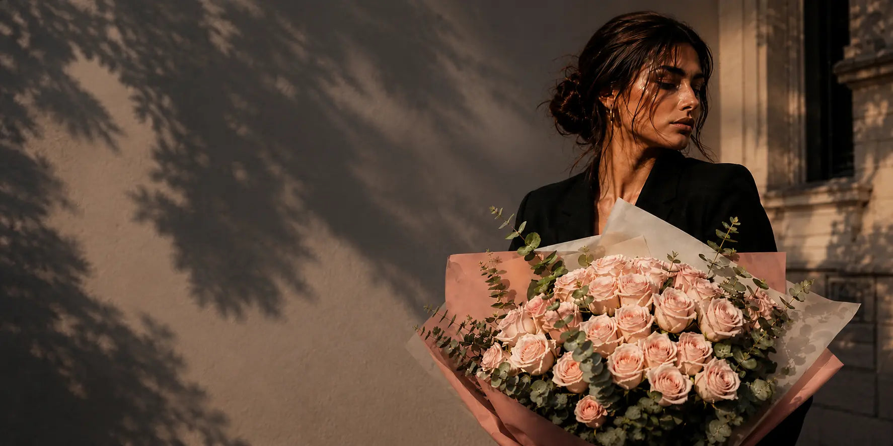 Mulher elegante com um grande ramo de rosas cor-de-rosa premium QRoses, fotografada ao ar livre com luz dourada ao final da tarde.