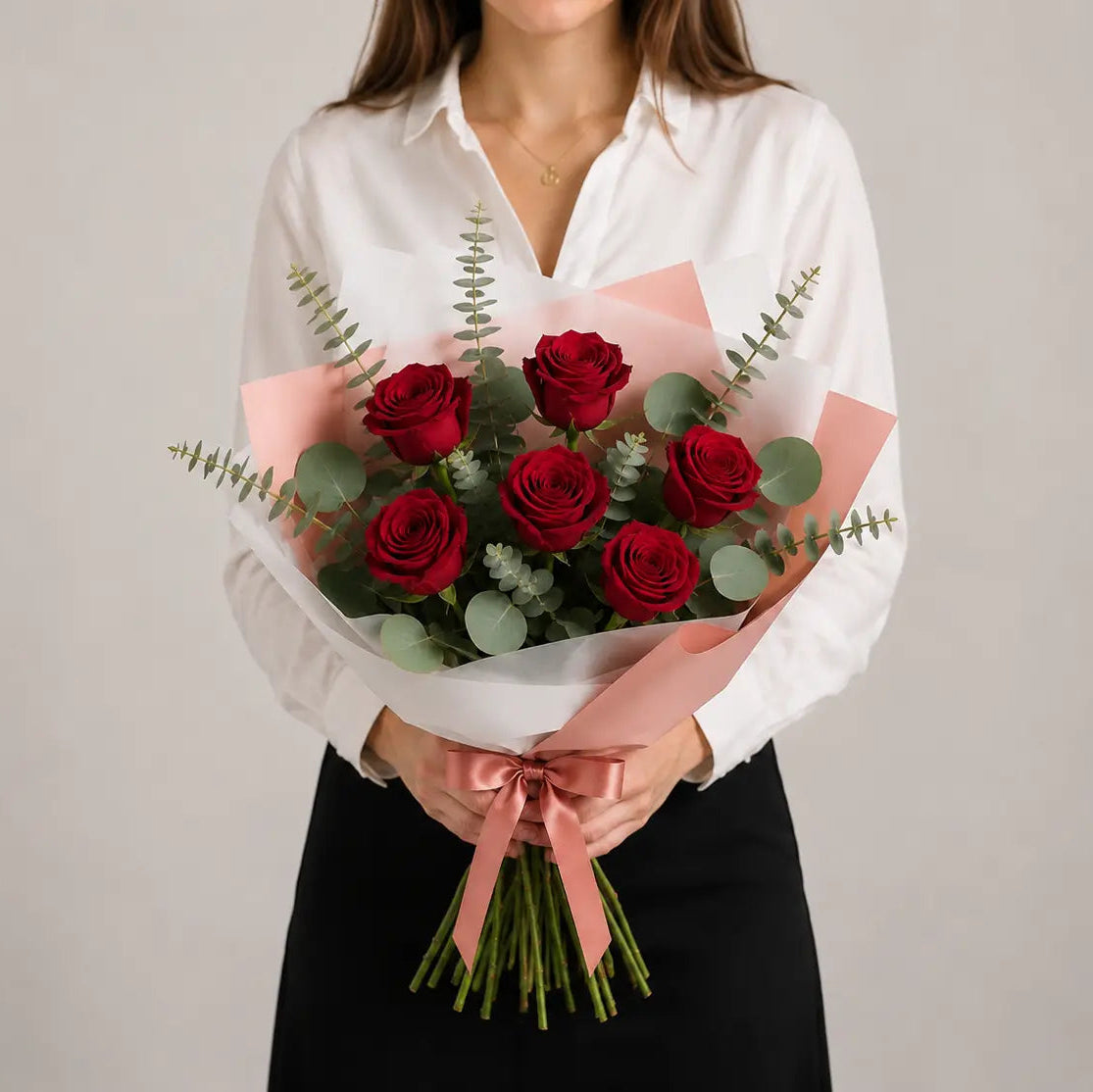 Modelo a segurar um Ramo Essencial de 5 ou 6 Rosas Vermelhas da QRoses, embalado com papel artístico e laço premium.