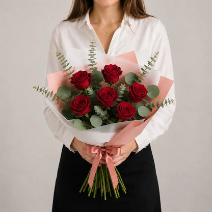 Modelo a segurar um Ramo Essencial de 5 ou 6 Rosas Vermelhas da QRoses, embalado com papel artístico e laço premium.