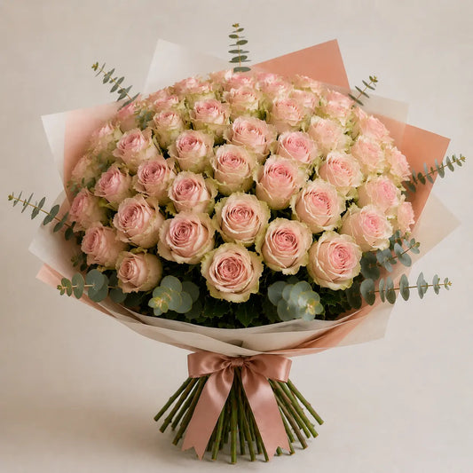 Ramo premium de rosas rosadas com bordes esverdeados, papel elegante, folhagem de eucalipto e laço rosa.