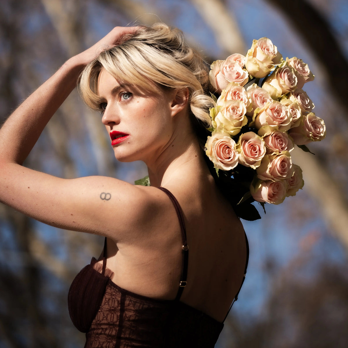 Elegant woman holding a bouquet of premium peach roses over her shoulder in an artistic outdoor portrait, showcasing luxury floral gifting by QRoses.